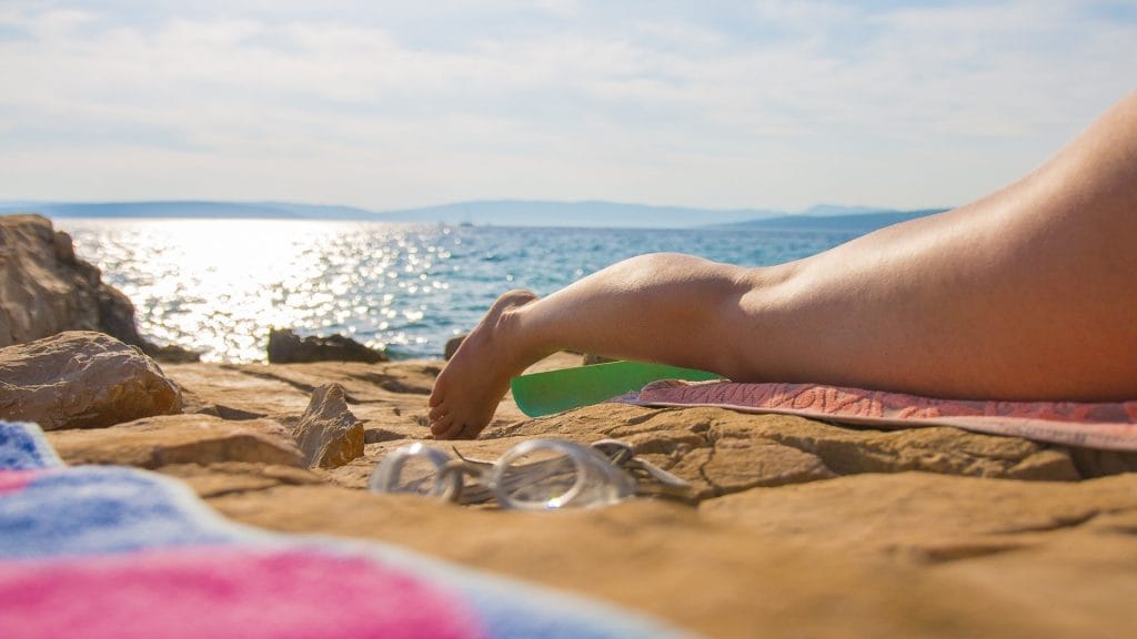 Sun-kissed legs with a spray tan on a beach, surrounded by soft sand and gentle waves.